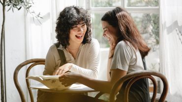 cheerful diverse girlfriends reading document at table