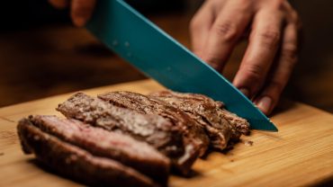 person slicing meat on brown chopping board